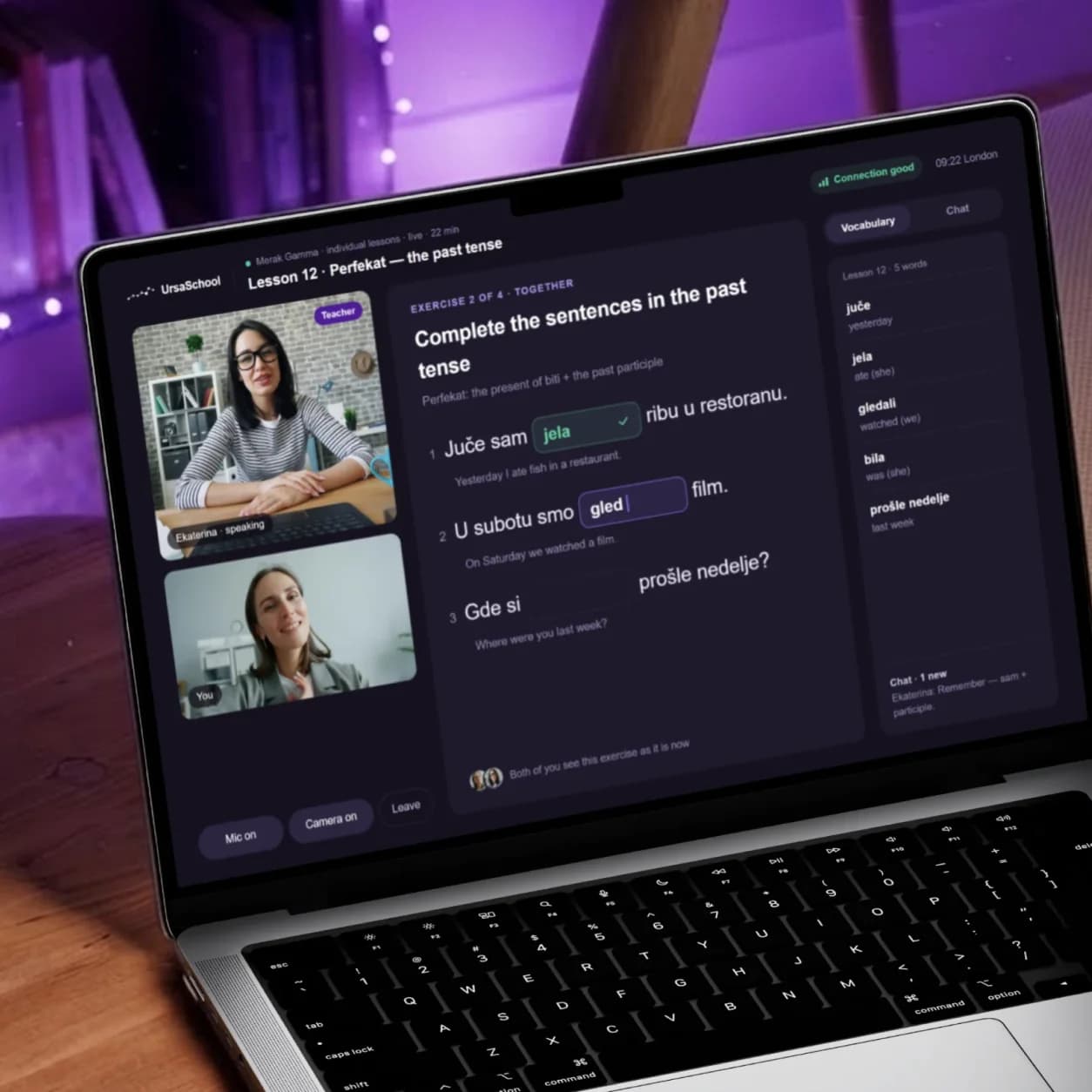 An Ursa School lesson on a laptop: the teacher and the student on video, a shared past-tense exercise the student is filling in, and the lesson's vocabulary beside it.